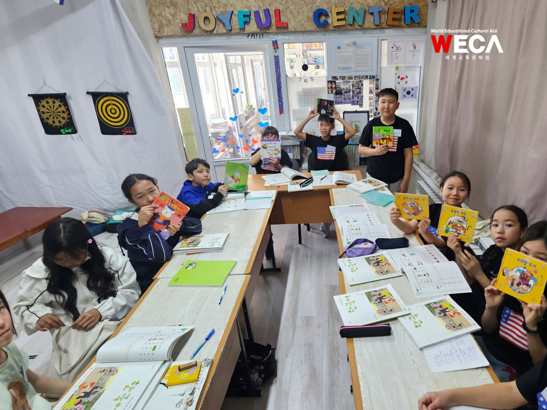 한국어 동화책을 한 권씩 소중하게 손에 들고 나란히 서서 카메라를 향해 환하게 웃고 있는 수업반 아이들의 모습