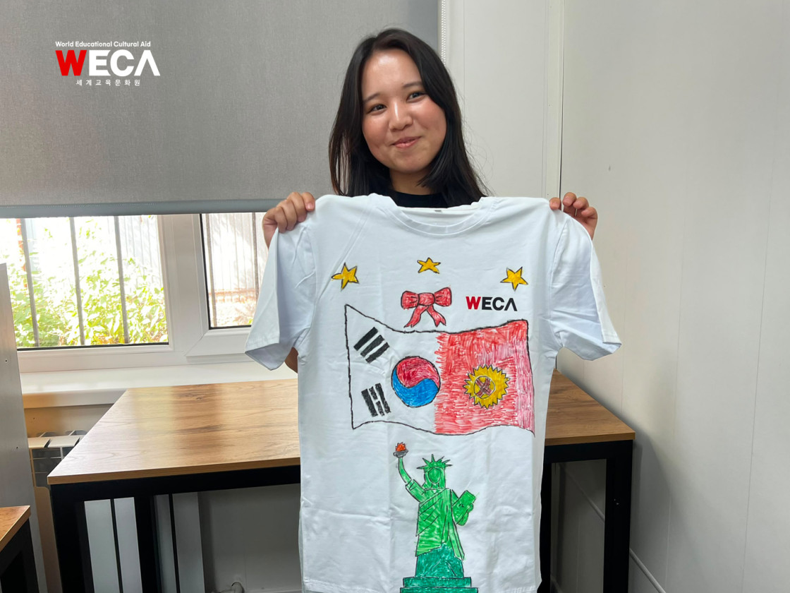 키르기스스탄 국기와 한국국기를 그린 티셔츠를 들고 웃는 WECA어학당 학생