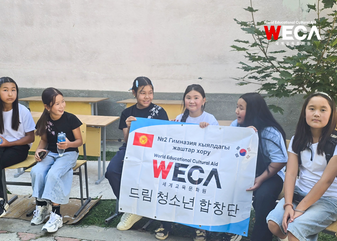 WECA 드림 청소년 합창단 현수막을 들고 웃으며 카메라를 쳐다보는 아이들
